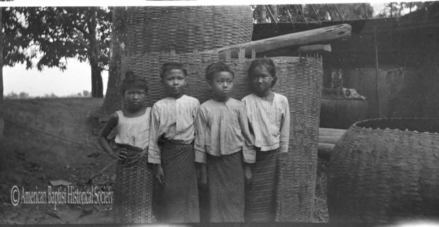 Four Burmese girls at Thabaung [Irrawaddy Division]. The large baskets are filled with [rice] paddy. April 2, 1923. 