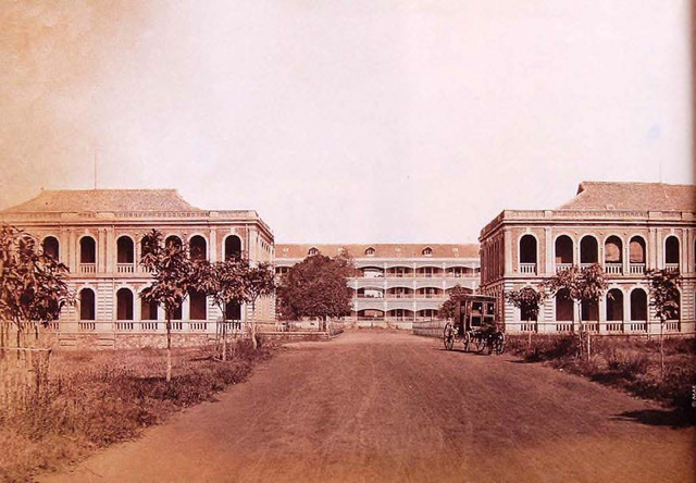 Fig. 4. Colonial Navy Grounds, 1882. The road in front with the building at the center is Ðinh Tiên Hoàng Street. Parts of the buildings on the left (which belonged to the College of Pharmacy) and right still exist. The resolution of the image is very high, as though by “zooming” one would see that, in the middle building, a sailor in white is staring at the photographer, while on the left a gardener brings water under the tree.