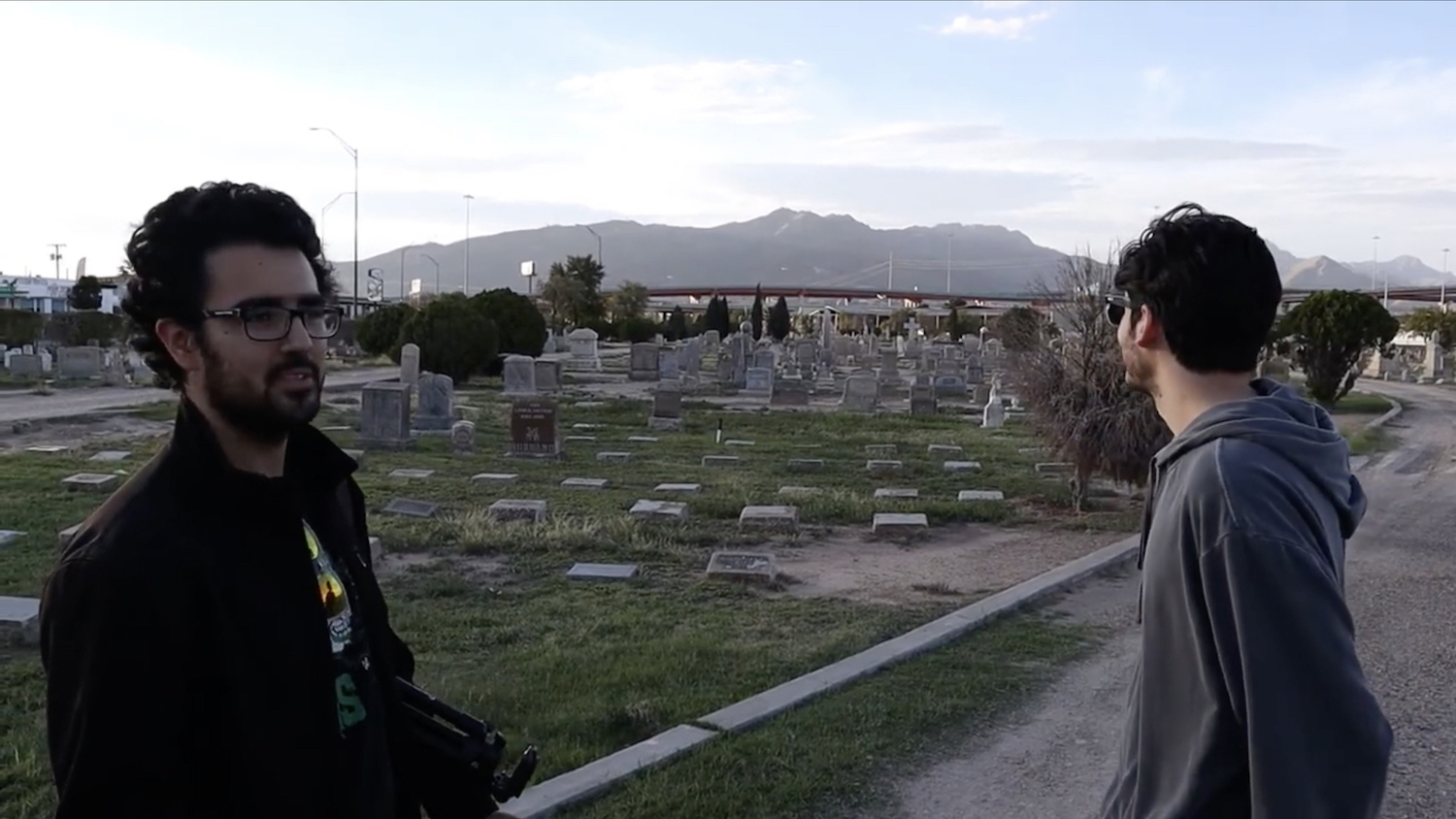 Figure 4. Screenshot of scene in “Haunting the Truth” (Dir. Eugenio Cantu), in which two of the protagonists—members of a film crew trying to capture filmed evidence of the existence of ghosts in the historic Concordia Cemetery—alternate idly gazing at the Sierra Juarez range and the I-10 Freeway as they figure out their next steps. Courtesy of director. Figure 4. Screenshot of scene in “Haunting the Truth” (Dir. Eugenio Cantu), in which two of the protagonists—members of a film crew trying to capture filmed evidence of the existence of ghosts in the historic Concordia Cemetery—alternate idly gazing at the Sierra Juarez range and the I-10 Freeway as they figure out their next steps. Courtesy of director.
