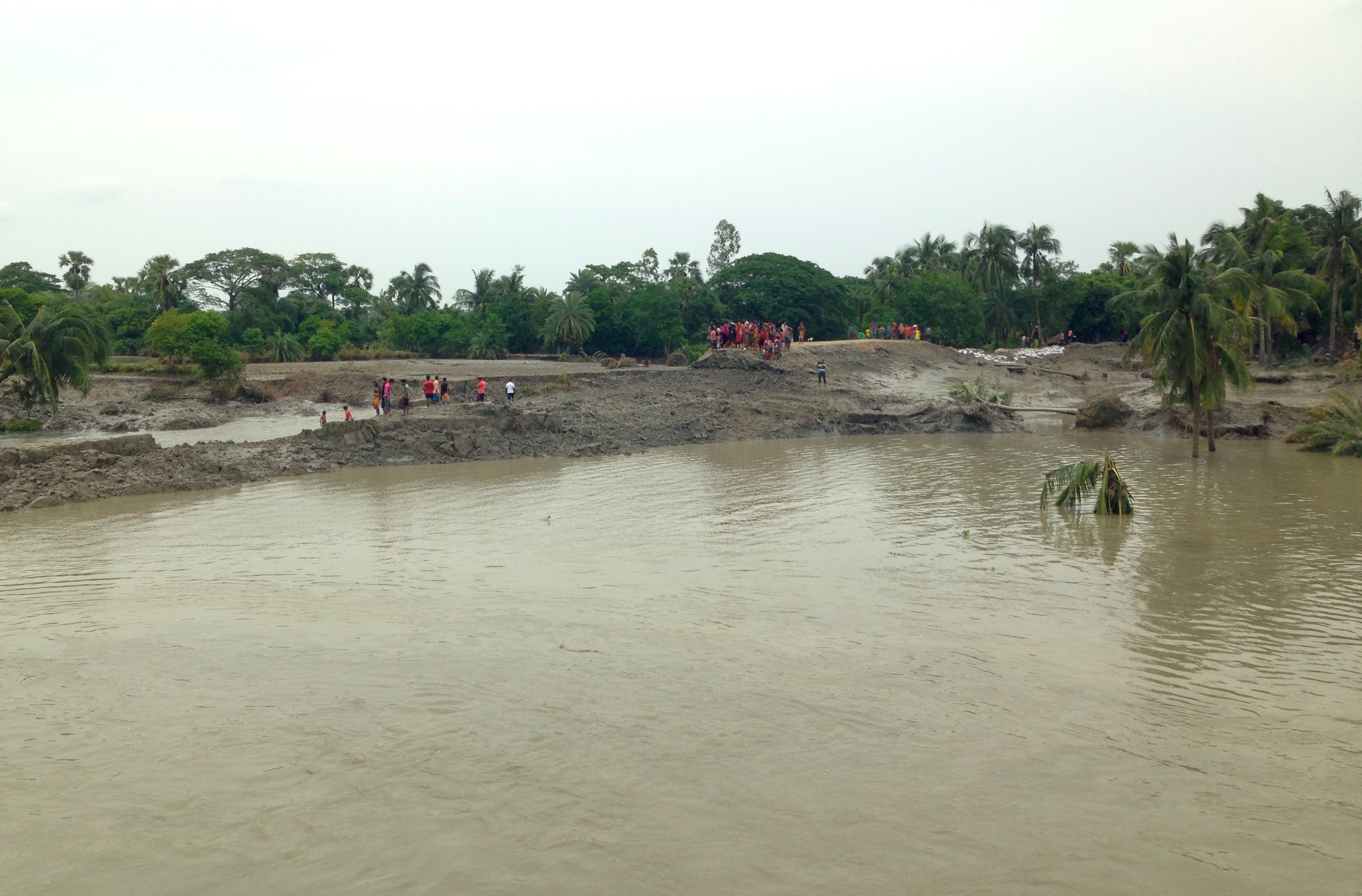 Figure 3. A crowd gathers at the top of the polder wall: A crowd assembled at the highest point of the embankment to survey the inundation. The embankment used to extend from where the residents stand on the far side of the Buribhodra River to where the viewer is looking out. The flooded site was previously traversable by elevated roadway. Following the destruction of the polder wall, the distance is impassable. Area inhabitants estimate that the water will not retreat for months. Figure 3. A crowd gathers at the top of the polder wall: A crowd assembled at the highest point of the embankment to survey the inundation. The embankment used to extend from where the residents stand on the far side of the Buribhodra River to where the viewer is looking out. The flooded site was previously traversable by elevated roadway. Following the destruction of the polder wall, the distance is impassable. Area inhabitants estimate that the water will not retreat for months.