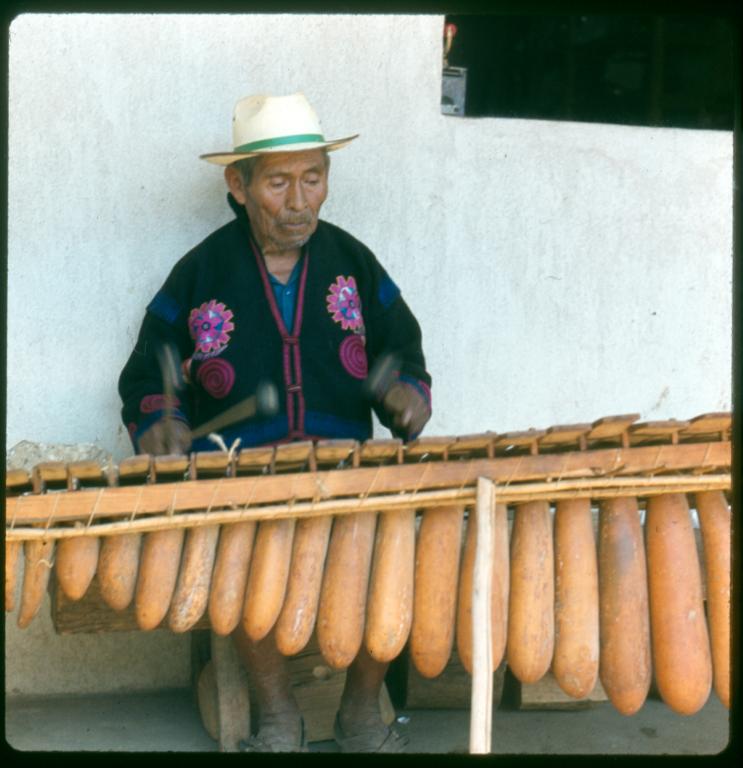 Figure 1. K’iche’ musicians playing a k’ojom, a marimba de tecomates (gourd marimba), in Chichicastenango, Guatemala. Note the gourd resonators and the evenly spaced single row of the keys. Photograph by Robert Garfias (reproduced with permission). Figure 1. K’iche’ musicians playing a k’ojom, a marimba de tecomates (gourd marimba), in Chichicastenango, Guatemala. Note the gourd resonators and the evenly spaced single row of the keys. Photograph by Robert Garfias (reproduced with permission).