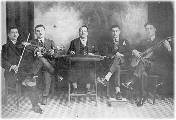 Photograph 1. A typical “Smyrna-style” ensemble consisting of violin, mandolin, santur and guitar. Note how the guitarist’s playing position and the footstool of singer Kostas Nuros reflect the influence of Western classical music. The photograph was taken in 1928. Photograph 1. A typical “Smyrna-style” ensemble consisting of violin, mandolin, santur and guitar. Note how the guitarist’s playing position and the footstool of singer Kostas Nuros reflect the influence of Western classical music. The photograph was taken in 1928.