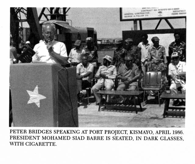 PETER BRIDGES SPEAKING AT PORT PROJECT, KISMAYO, APRIL 1986.  PRESIDENT MOHAMED SIAD BARRE IS SEATED, IN DARK GLASSES, WITH CIGARETTE.