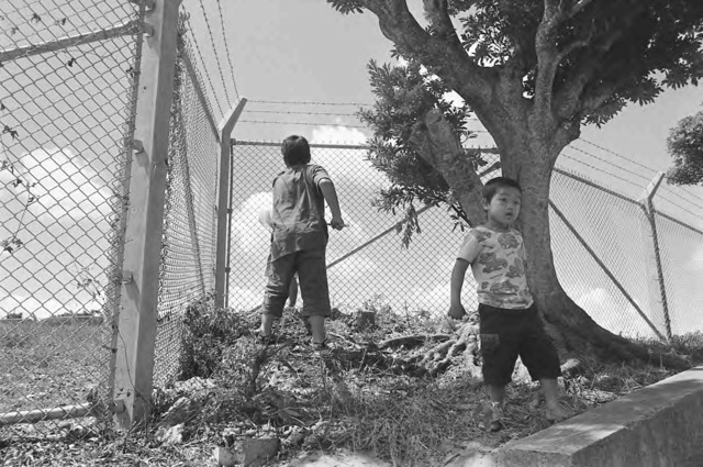 Mao Ishikawa, “Catching cicadas along the Futenma Air Base fence line. August 2009. Ginowan City, Okinawa”, from the Fences series, ©Mao Ishikawa. Mao Ishikawa, “Catching cicadas along the Futenma Air Base fence line. August 2009. Ginowan City, Okinawa”, from the Fences series, ©Mao Ishikawa.