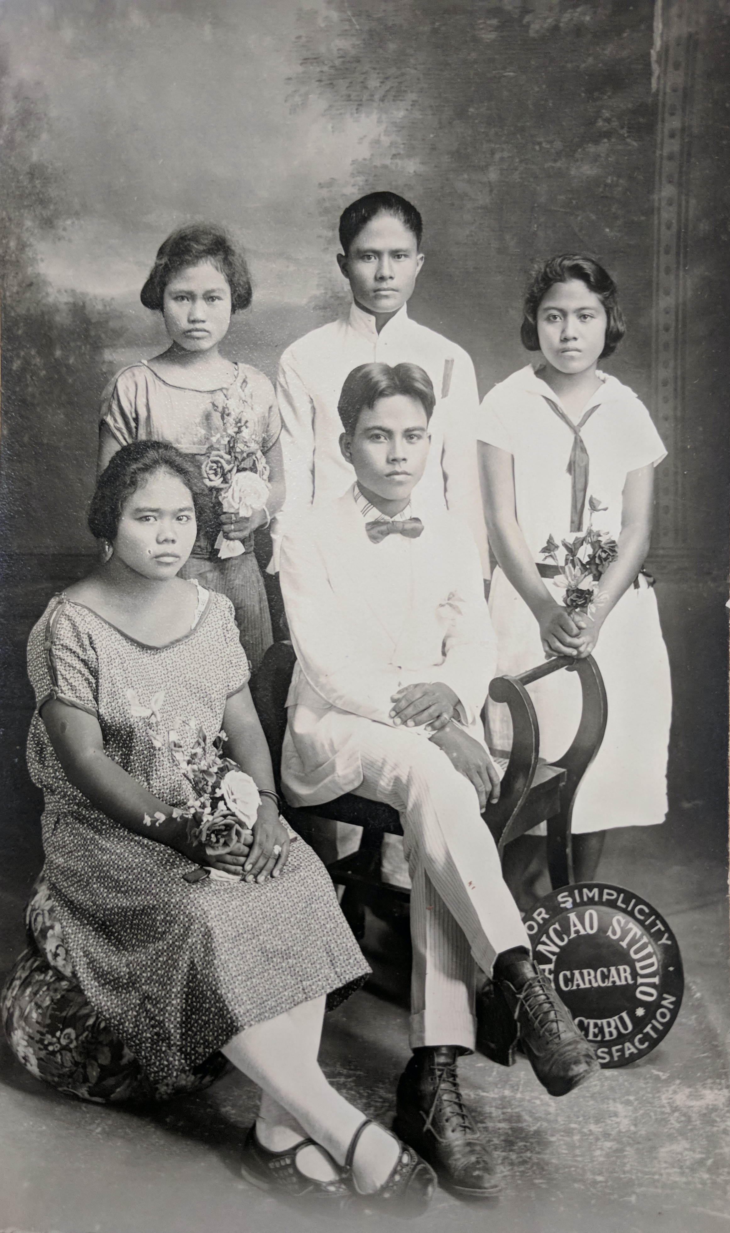 Alt-text: “Three girls and two boys in formalwear, with a Mancao Studios sign on the bottom right corner.” Alt-text: “Three girls and two boys in formalwear, with a Mancao Studios sign on the bottom right corner.”